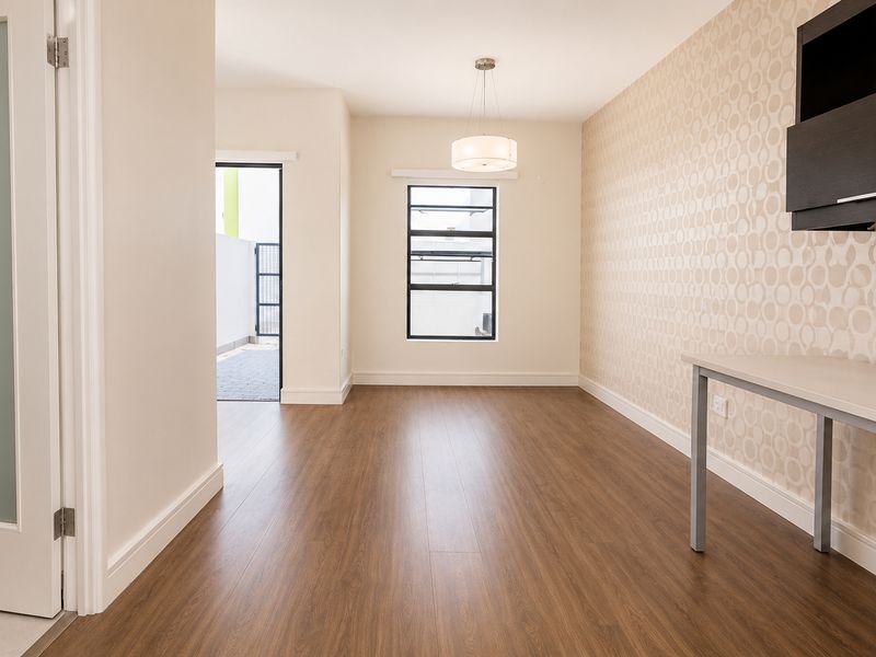 A bright, modern room featuring wood-look laminate flooring, patterned wallpaper, a built-in desk unit, and a frosted glass door leading to an adjacent space.