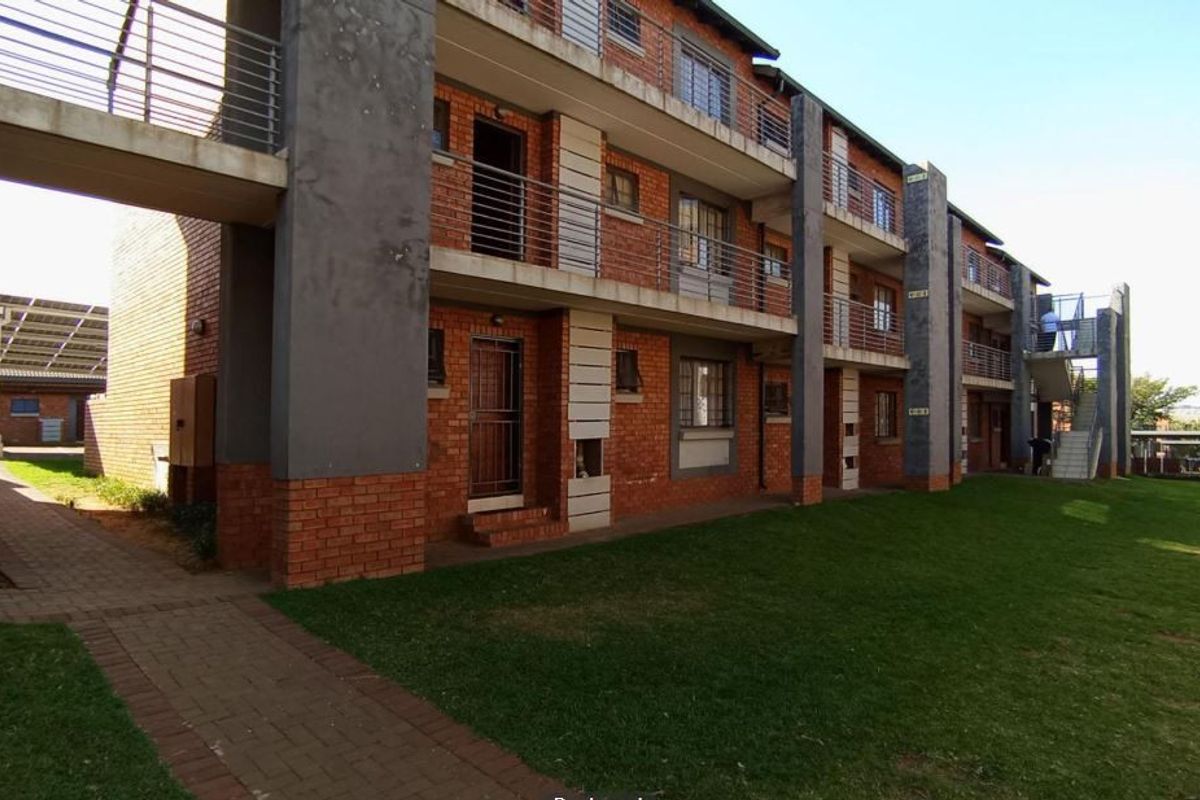 Exterior view of a multi-story apartment complex featuring brick facade, communal lawn, paved walkways, and balcony access for residents.