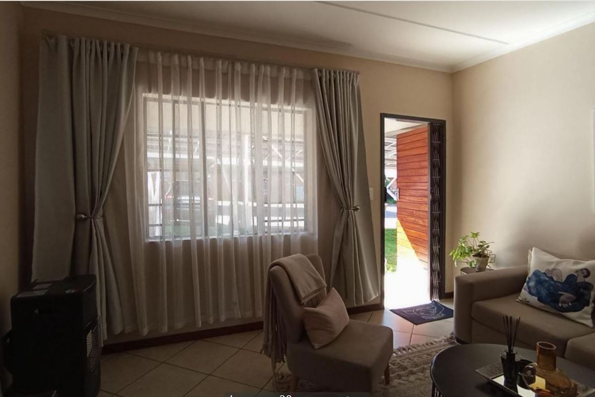 A comfortable living room featuring tiled flooring, a large window for natural light, and direct access to the exterior via a security gate.