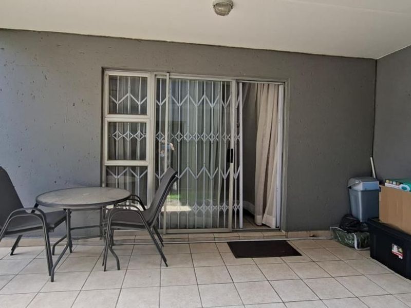 A covered patio area featuring tiled flooring, a sliding glass door with a security gate, and overhead lighting.
