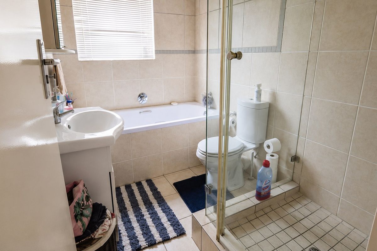 A functional bathroom featuring a bathtub, separate shower enclosure, toilet, and vanity basin with neutral wall and floor tiling.