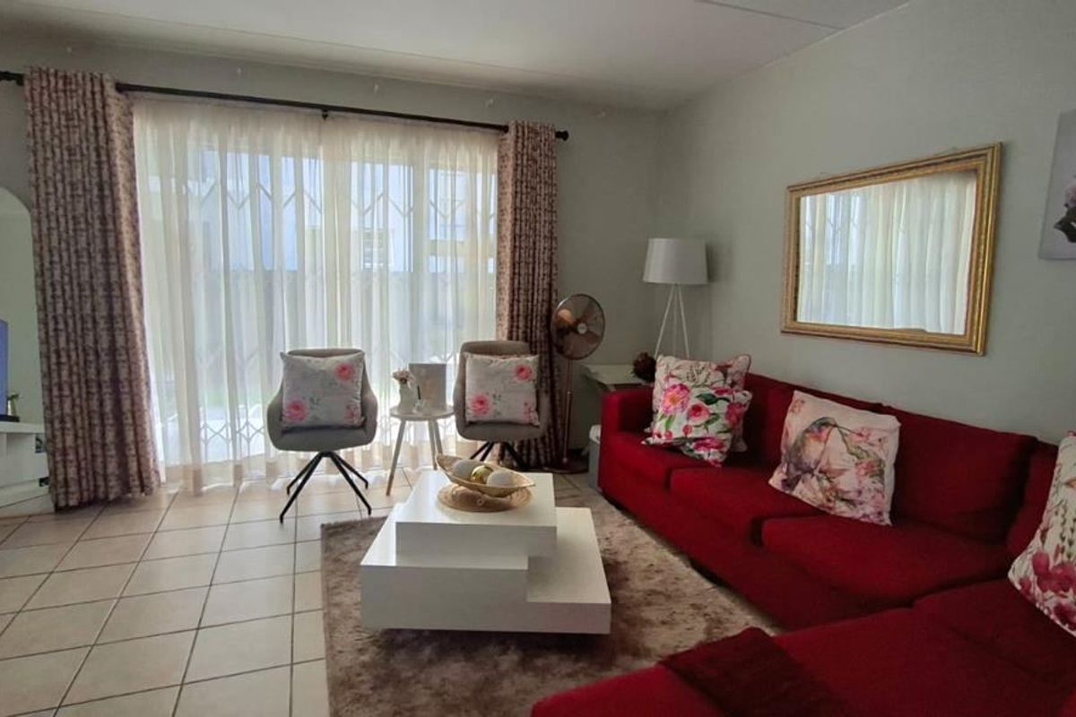 A comfortable living room featuring tiled flooring and a large sliding glass door with a security gate, providing access to the outdoor area.