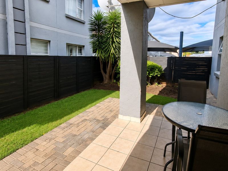 A well-maintained covered patio area featuring tiled flooring, adjacent to a private garden with paved pathways and modern timber fencing.