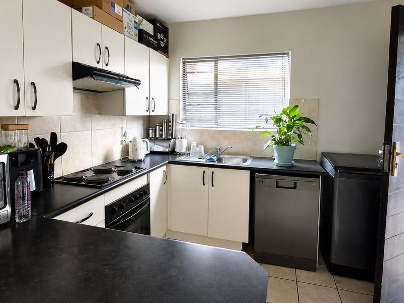 Functional kitchen featuring white cabinetry, dark laminate countertops, built-in oven, electric hob, extractor fan, and tiled backsplash with neutral floor tiles.