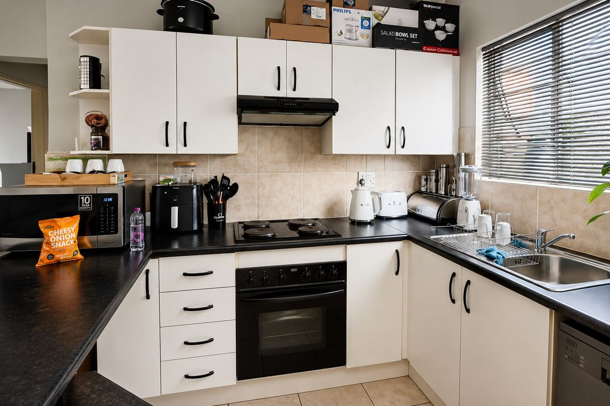 A functional kitchen featuring white cabinetry, black countertops, a built-in oven with electric hob, and a stainless steel sink with tiled backsplash.