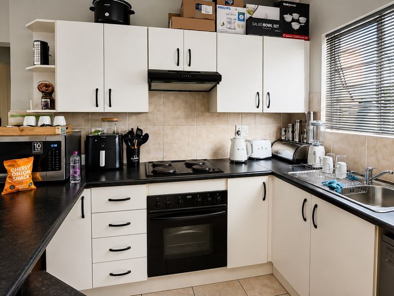 A functional kitchen featuring white cabinetry, black countertops, a built-in oven with electric hob, and a stainless steel sink with tiled backsplash.