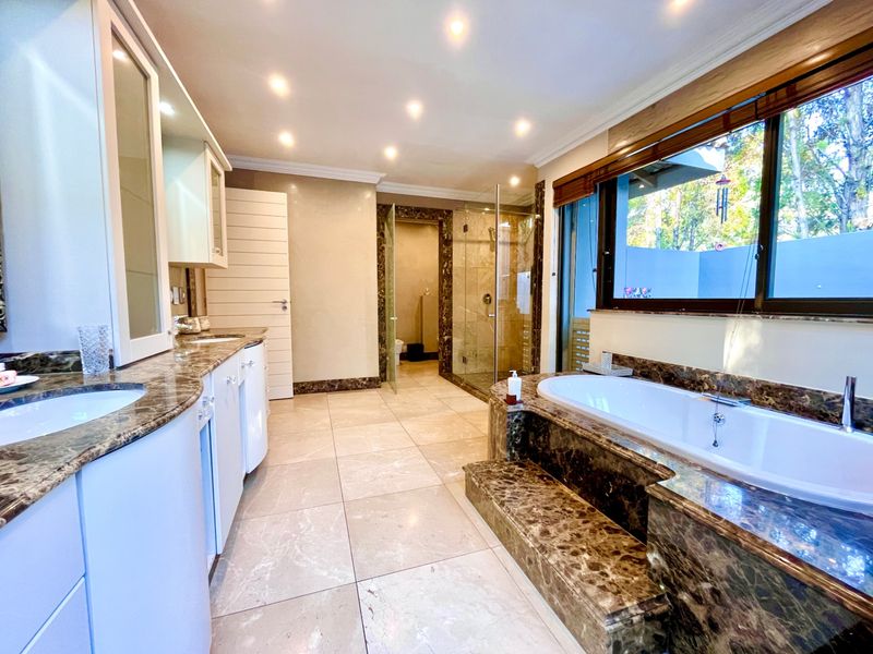 Spacious bathroom featuring a built-in soaking tub with marble surround, dual vanity with marble countertop, and a glass-enclosed walk-in shower.