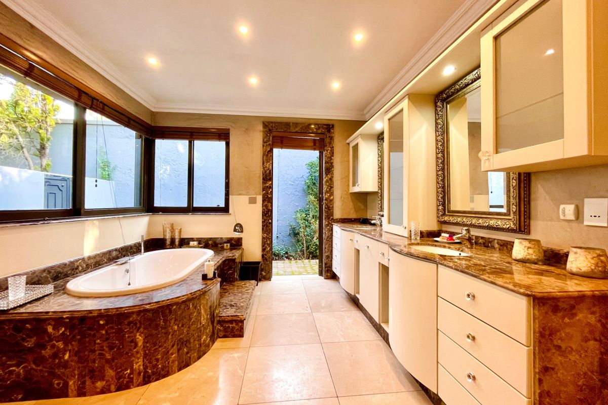 Spacious bathroom featuring a built-in marble-clad bathtub, dual vanity with marble countertops, recessed lighting, and direct access to a private outdoor courtyard.