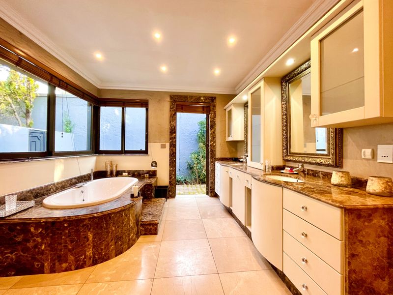 Spacious bathroom featuring a built-in marble-clad bathtub, dual vanity with marble countertops, recessed lighting, and direct access to a private outdoor courtyard.