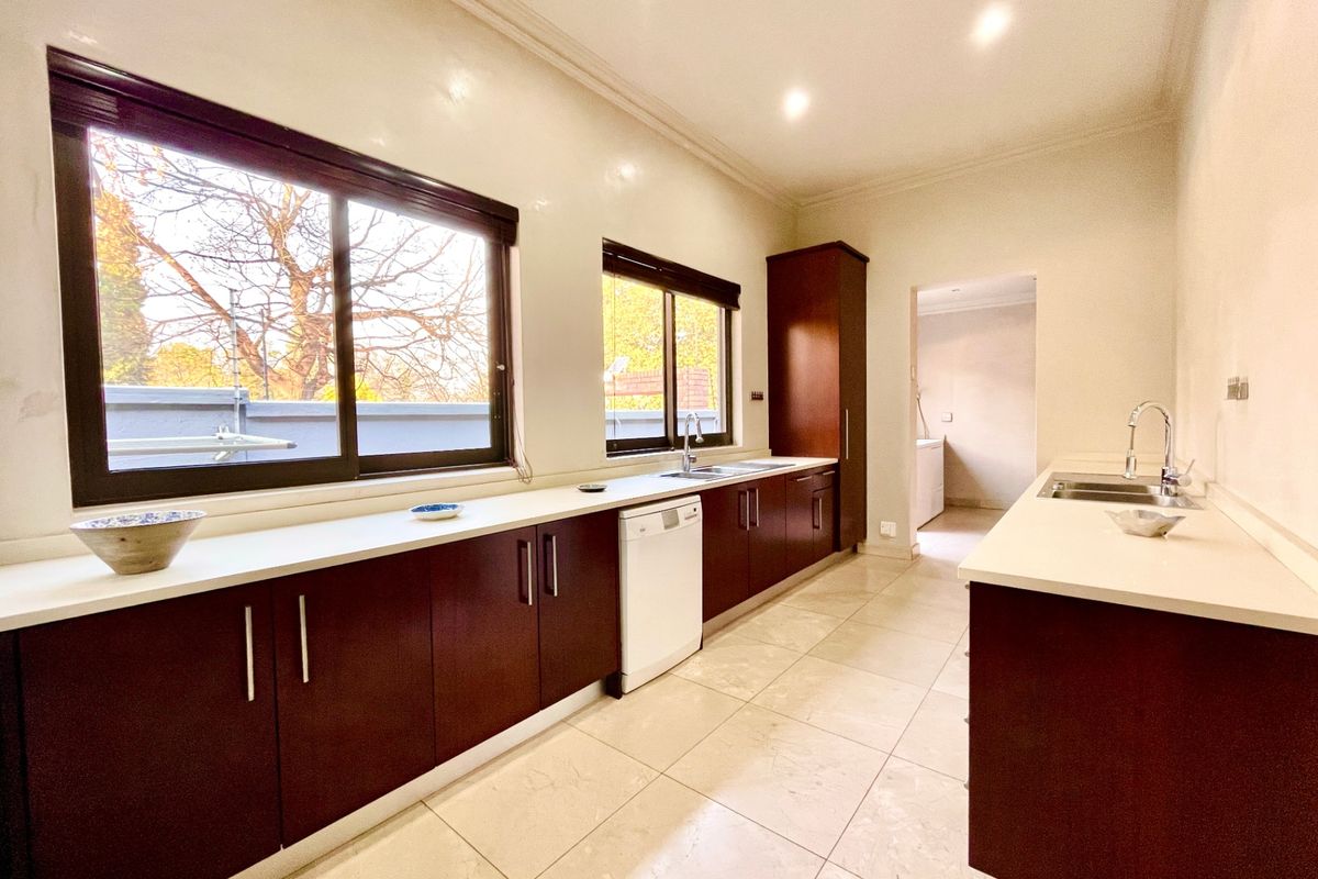 A spacious, modern kitchen featuring dark wood cabinetry, light stone countertops, tiled flooring, and large windows providing ample natural light.