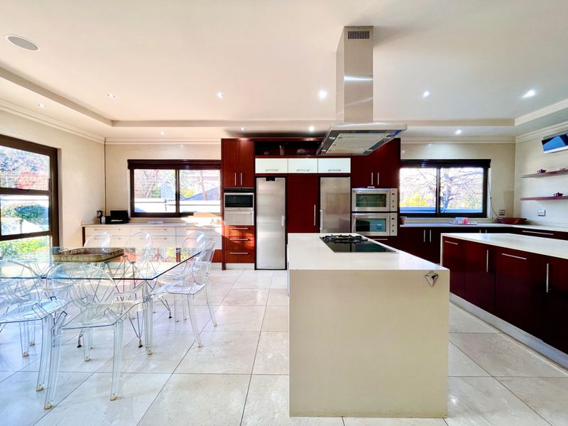 Spacious open-plan kitchen featuring dark wood cabinetry, a large central island with a built-in hob, stainless steel extractor fan, and integrated wall ovens.