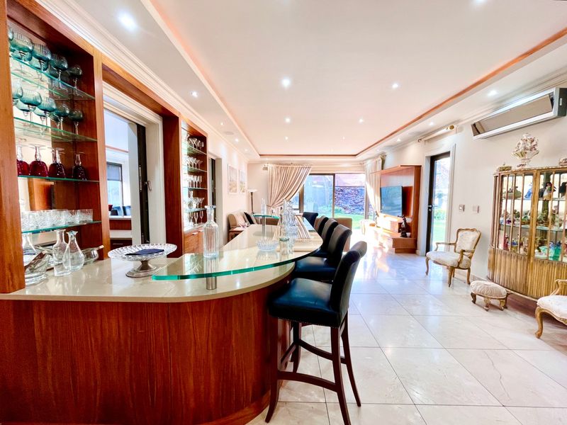 Spacious open-plan living area featuring a custom built-in wooden bar with glass countertop, recessed lighting, and tiled flooring throughout.
