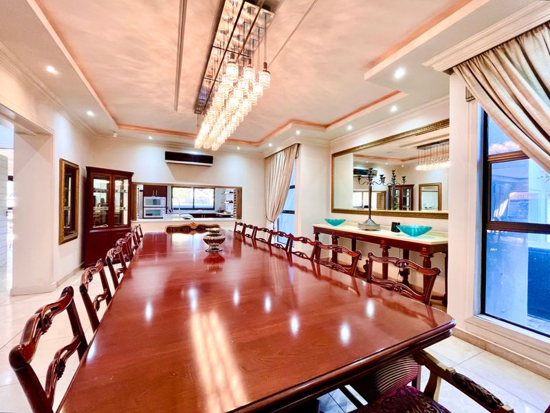 Spacious formal dining room featuring a large central chandelier, recessed ceiling lighting, and a serving window connecting to the kitchen area.