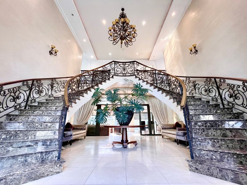 Grand double staircase with ornate wrought iron railings and marble steps, creating an impressive entrance hall with high ceilings and elegant lighting.
