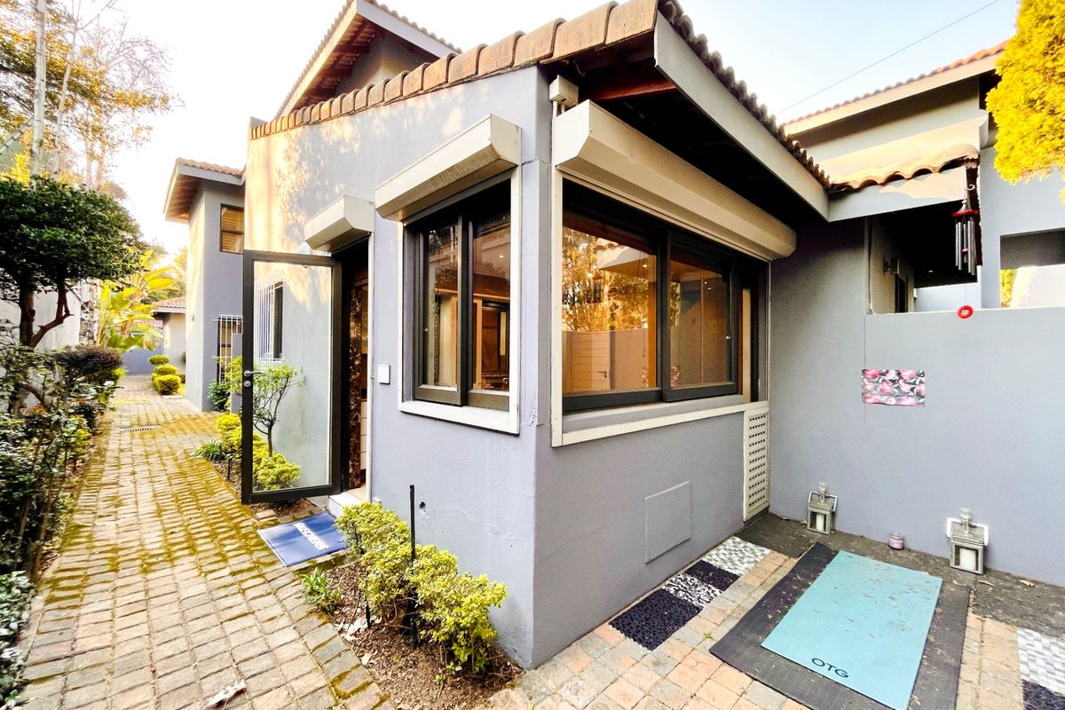 Exterior view of the property featuring a paved walkway, grey rendered walls, and dark-framed windows with integrated security shutters.