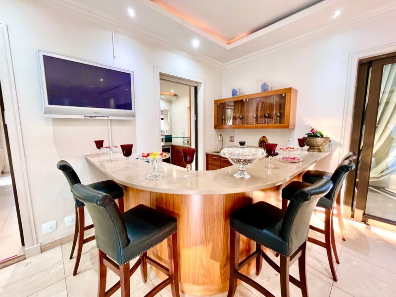 A well-appointed home bar area featuring a curved stone countertop, built-in cabinetry, recessed ceiling lighting, and tiled flooring.