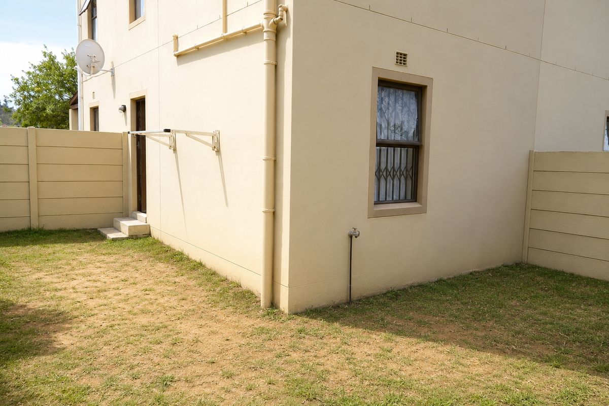 A view of the rear exterior of the property featuring a small private garden, boundary wall, and external plumbing fixtures.
