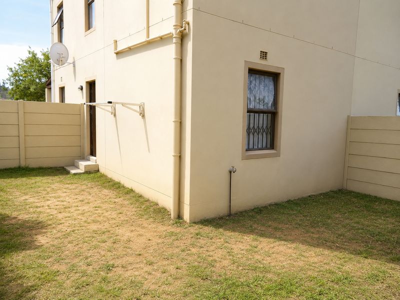 A view of the rear exterior of the property featuring a small private garden, boundary wall, and external plumbing fixtures.