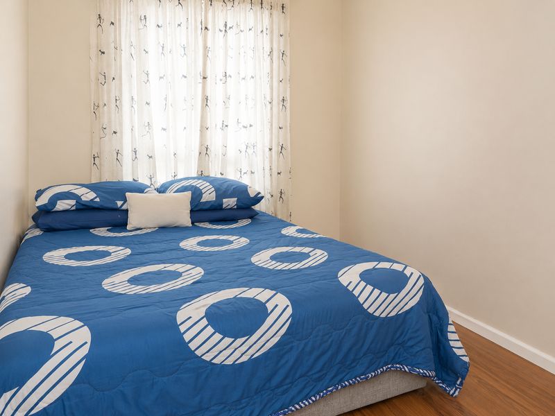 A cozy bedroom featuring warm-toned laminate flooring and a window dressed with patterned curtains.