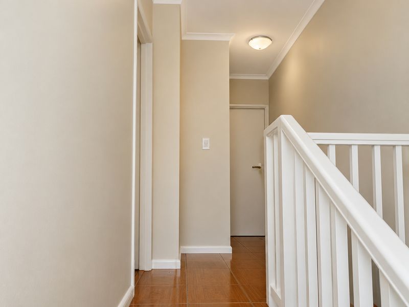 A bright and clean hallway featuring tiled flooring, neutral wall tones, and a white timber staircase balustrade leading to the upper level.