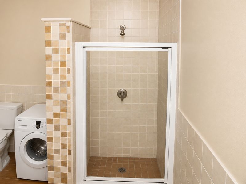 A functional bathroom featuring a tiled shower enclosure with a glass door, adjacent to a built-in laundry area with a washing machine.