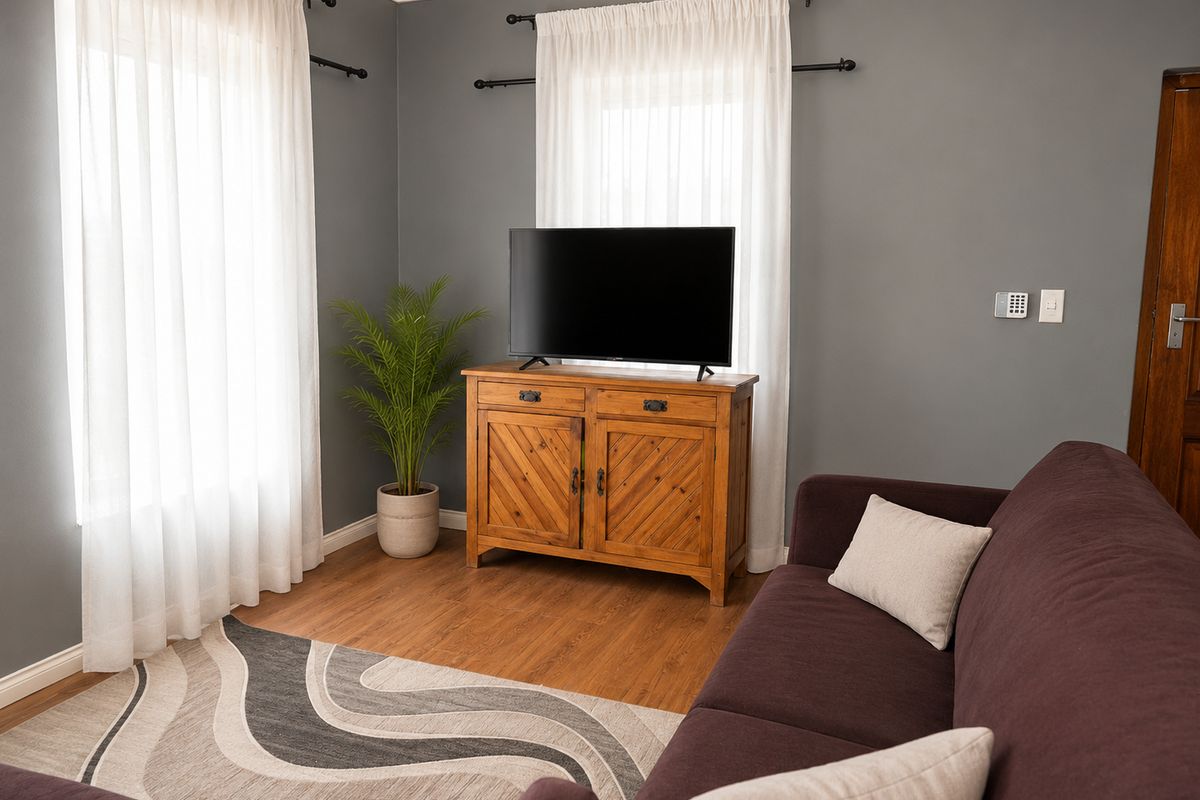 A comfortable living room featuring wood-look flooring, grey painted walls, and dual windows with curtain rods.