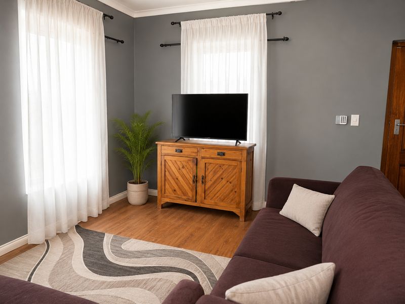 A comfortable living room featuring wood-look flooring, grey painted walls, and dual windows with curtain rods.