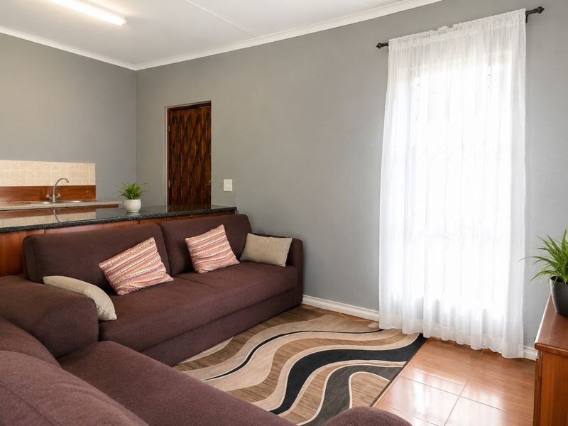 An open-plan living area featuring tiled flooring, neutral grey walls, and a compact kitchen counter with a sink and tiled splashback.