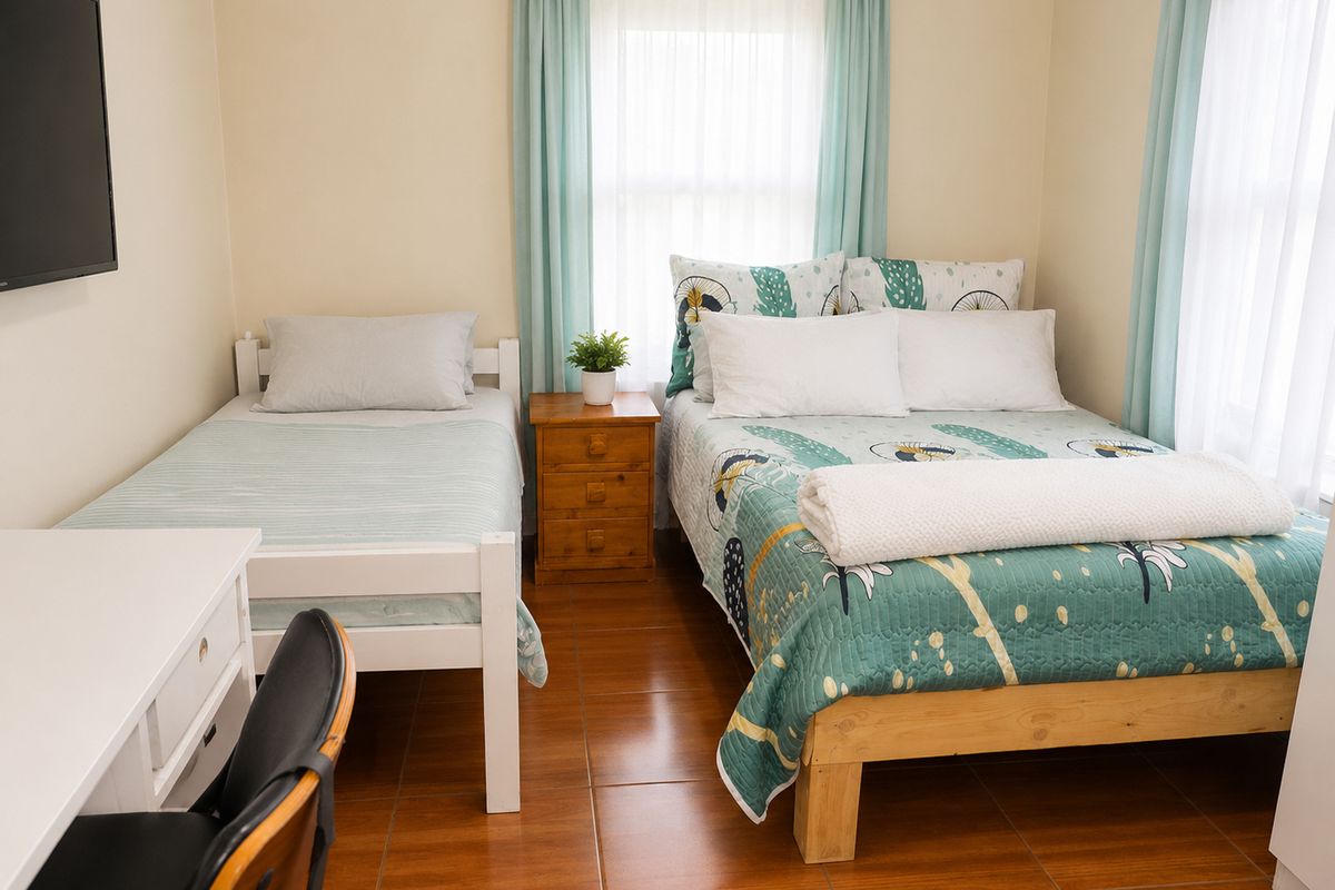 A bedroom featuring tiled flooring, dual windows with curtains, and a wall-mounted television.