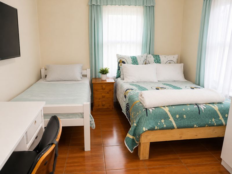 A bedroom featuring tiled flooring, dual windows with curtains, and a wall-mounted television.