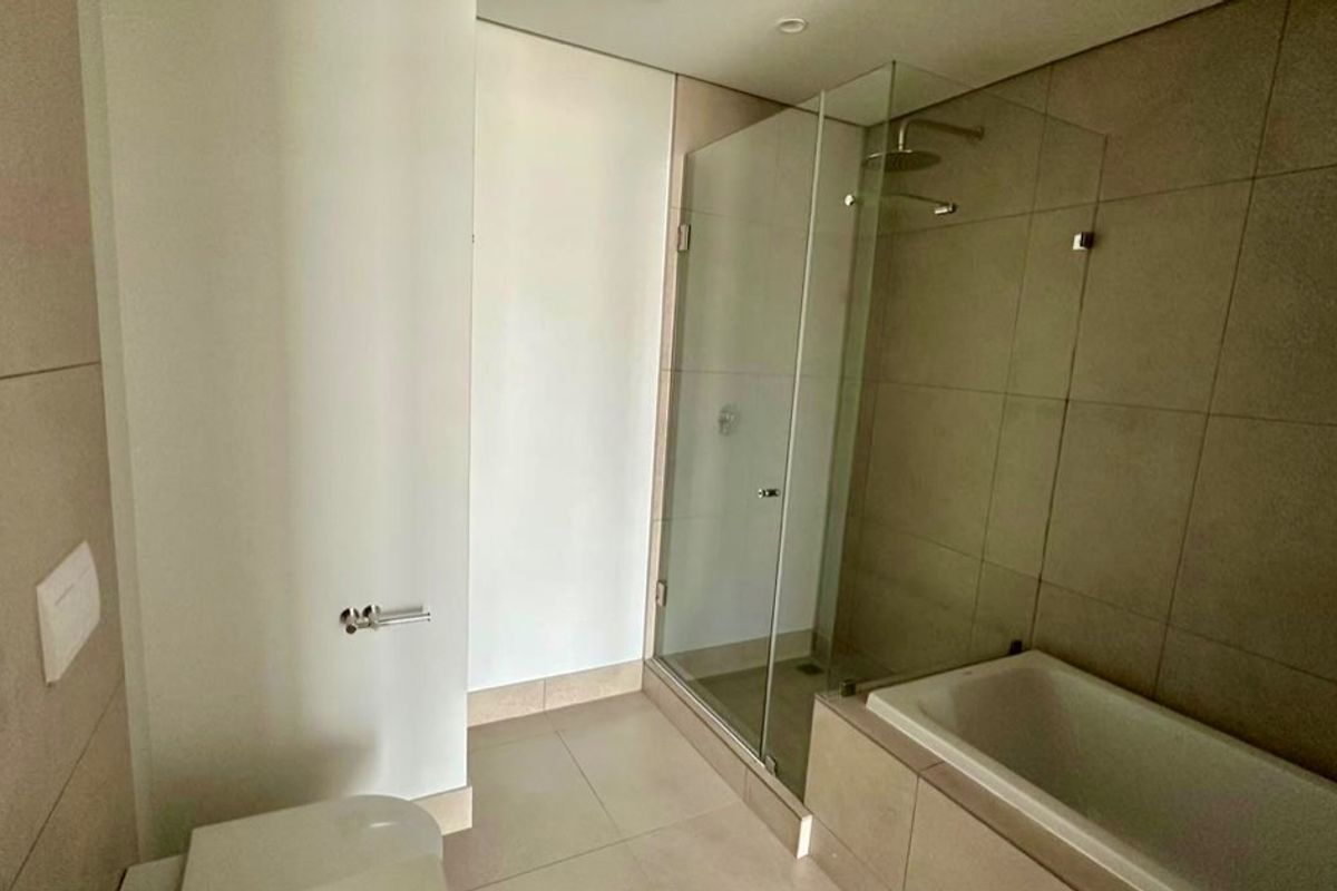 Modern bathroom featuring a walk-in glass shower, built-in bathtub, and neutral floor-to-ceiling tiling with contemporary fixtures.