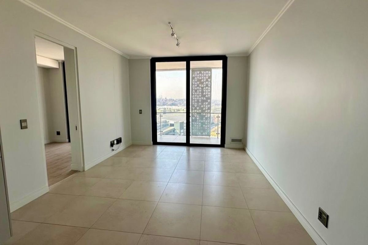 A bright, empty living area featuring large format floor tiles, neutral walls, and a sliding glass door leading to a balcony with city views.