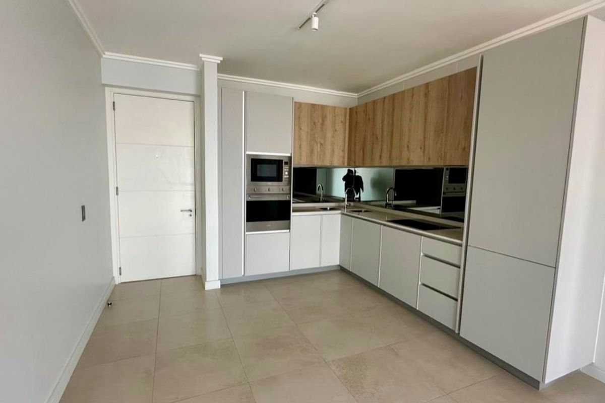 Modern kitchen featuring sleek cabinetry, built-in oven and microwave, mirror splashback, and neutral tiled flooring in an open-plan layout.