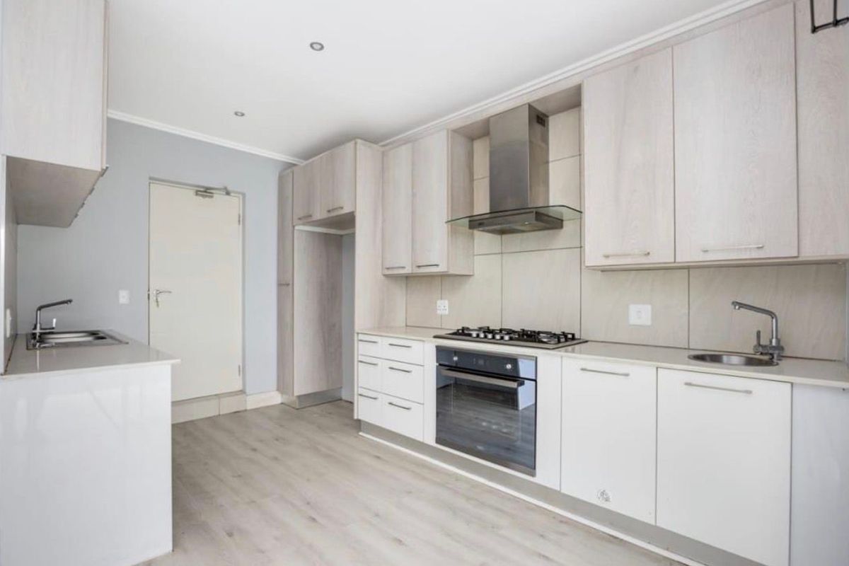 Modern kitchen featuring light wood-toned cabinetry, integrated gas hob, electric oven, extractor fan, and durable laminate flooring in a clean, open layout.