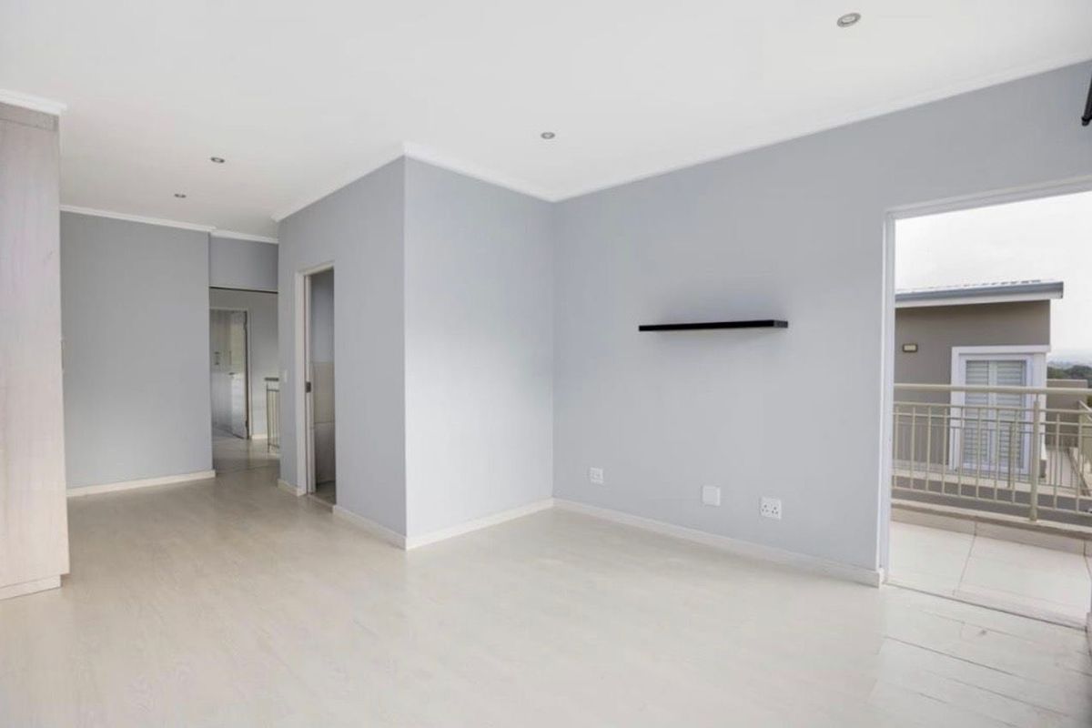 A bright, empty living area featuring neutral walls, laminate flooring, recessed lighting, and direct access to an outdoor balcony.