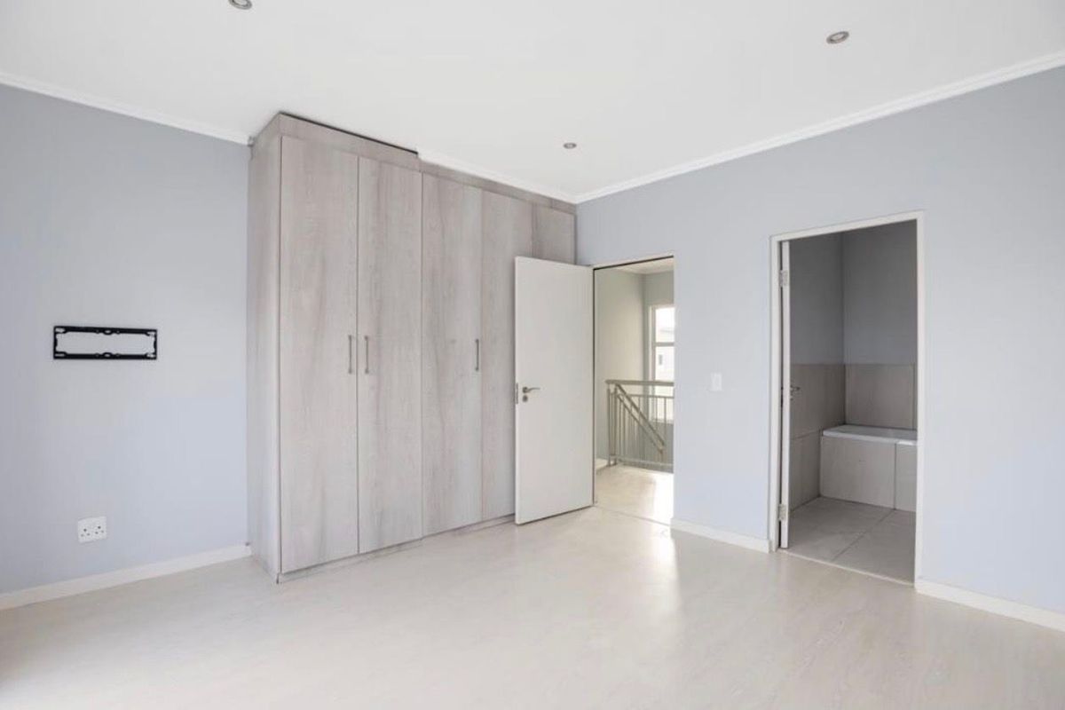 Spacious bedroom featuring neutral walls, light laminate flooring, built-in cupboards, and direct access to an en-suite bathroom.