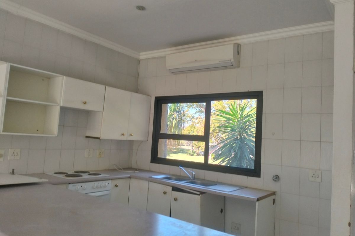 A functional kitchen featuring built-in cabinetry, a double sink, an electric hob, and a wall-mounted air conditioning unit.