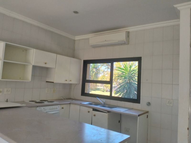 A functional kitchen featuring built-in cabinetry, a double sink, an electric hob, and a wall-mounted air conditioning unit.