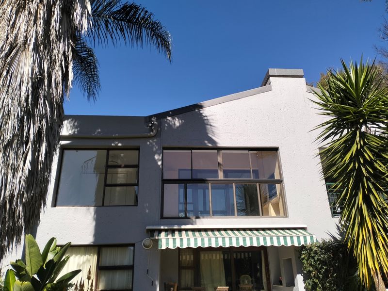 Rear elevation of the townhouse featuring large windows, a balcony, and a retractable striped awning over the ground floor patio area.