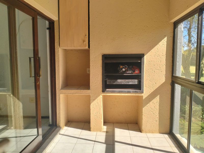 Covered patio area featuring a built-in braai, tiled flooring, and sliding glass doors providing access to the interior.