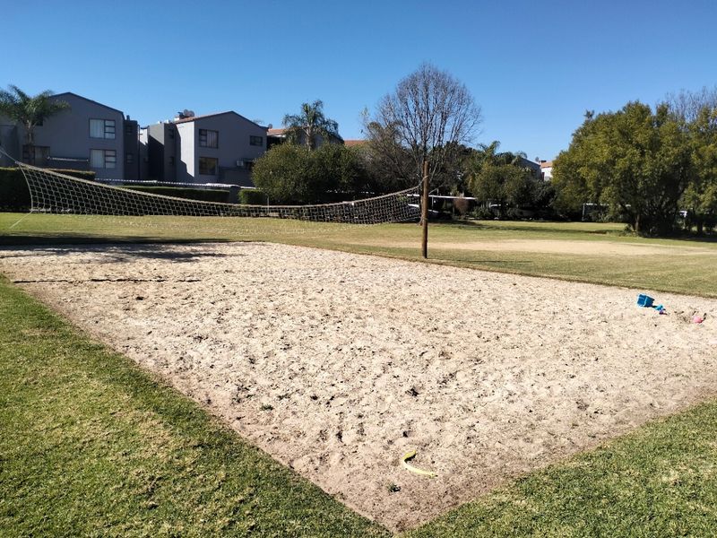 A communal outdoor sand volleyball court situated within a landscaped residential estate, featuring a net and surrounding lawn areas.