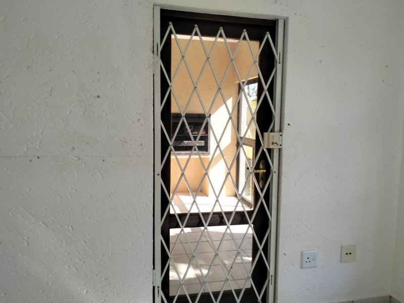 A view through a security gate leading to an outdoor patio area featuring a built-in braai.