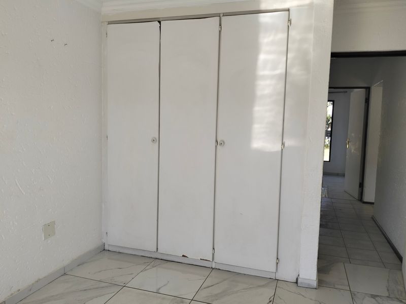 A bedroom interior featuring built-in white wardrobes with tiled flooring, leading into an adjacent hallway area.