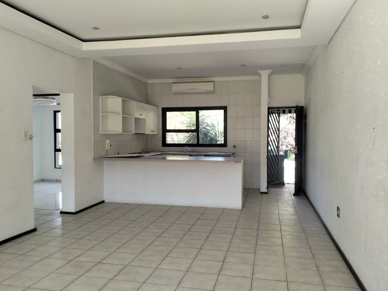 An open-plan kitchen area featuring a breakfast bar, tiled flooring, recessed ceiling detail, and direct access to an outdoor space.