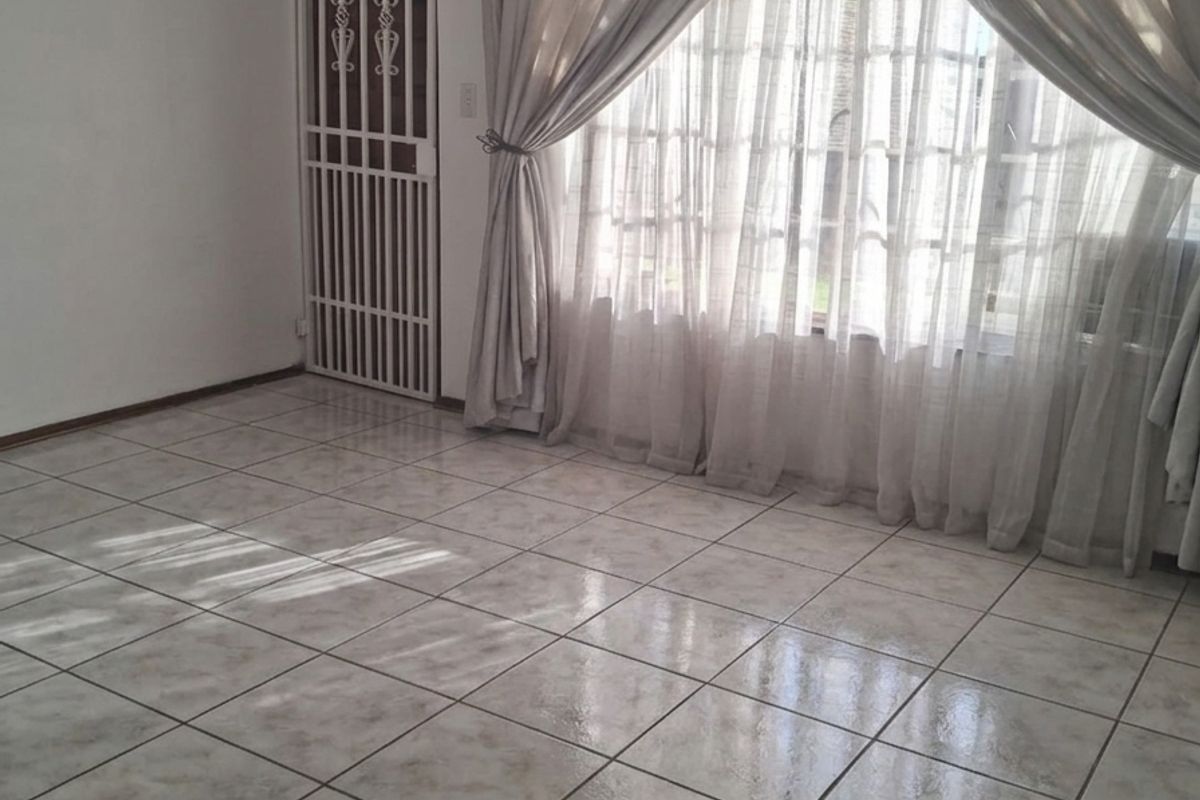 A bright, tiled living area featuring a ceiling fan and a security gate leading to the exterior.