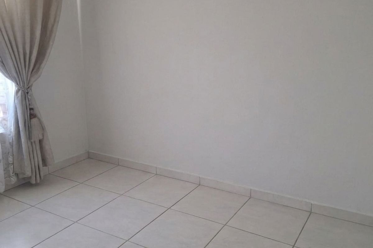 A bright, empty bedroom featuring neutral ceramic floor tiles and a window with installed curtain tracks.