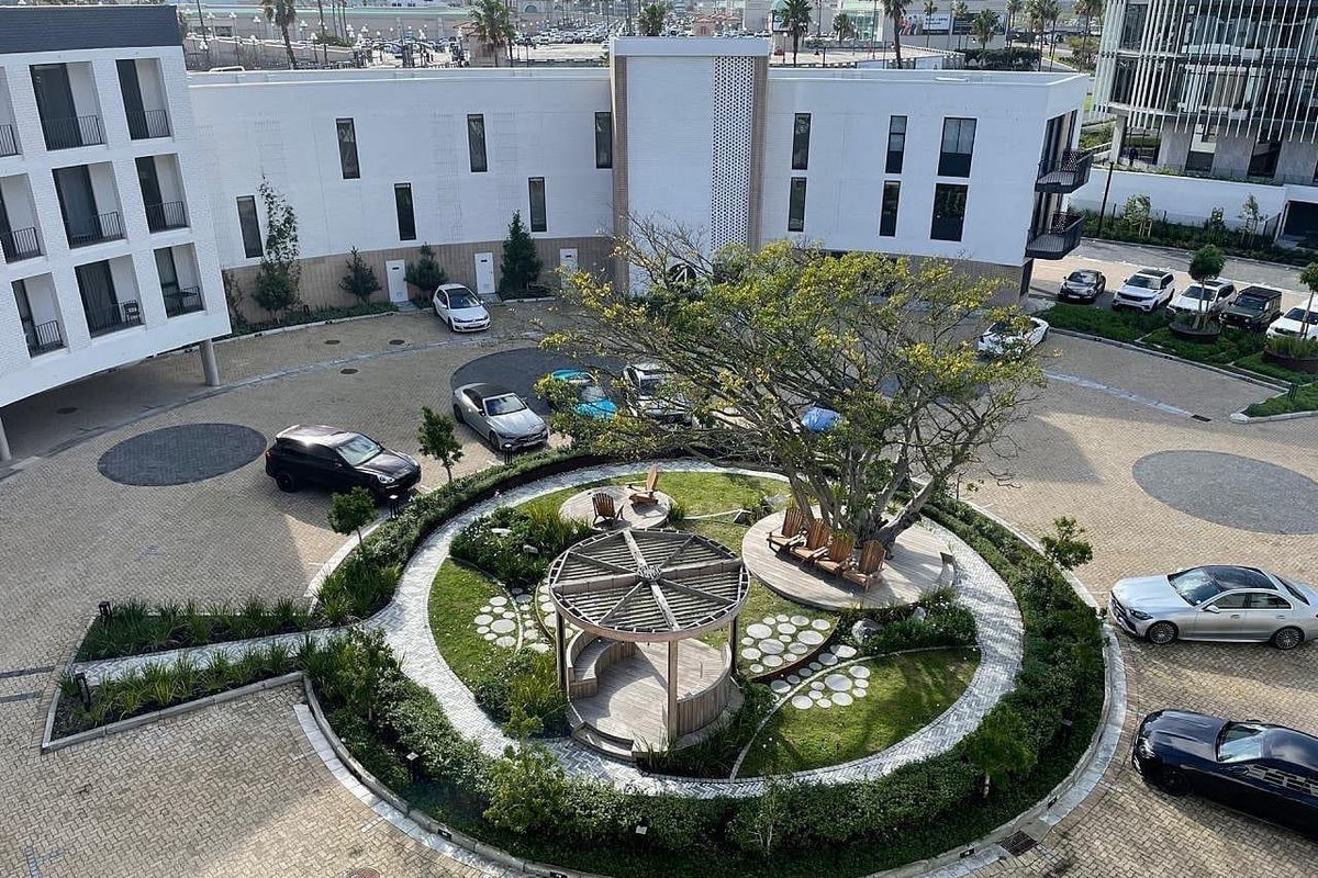 Aerial view of a modern apartment complex courtyard featuring a landscaped garden, central wooden gazebo, and paved driveway area.
