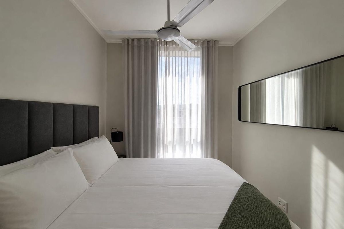 A well-maintained bedroom featuring a ceiling fan, neutral wall tones, and floor-to-ceiling curtains allowing natural light.