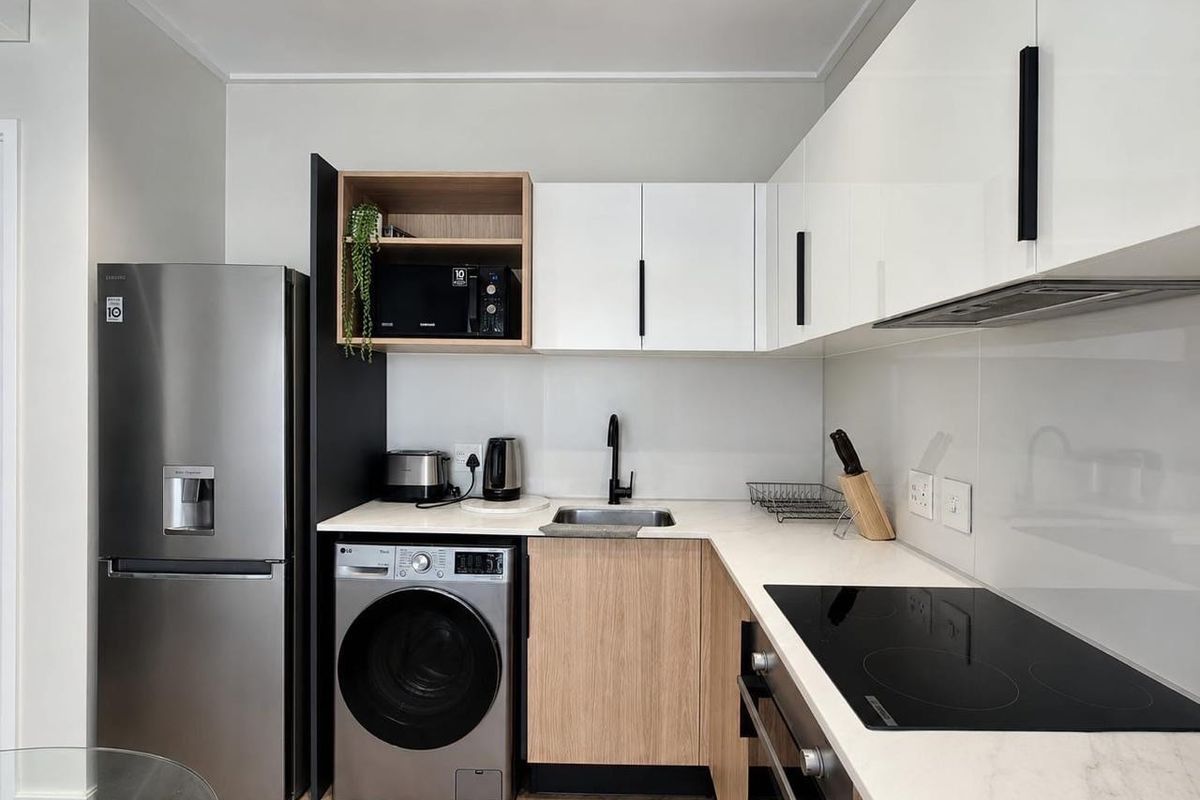 Modern compact kitchen featuring sleek white and wood-tone cabinetry, stone countertops, integrated appliances, and high-quality finishes throughout.