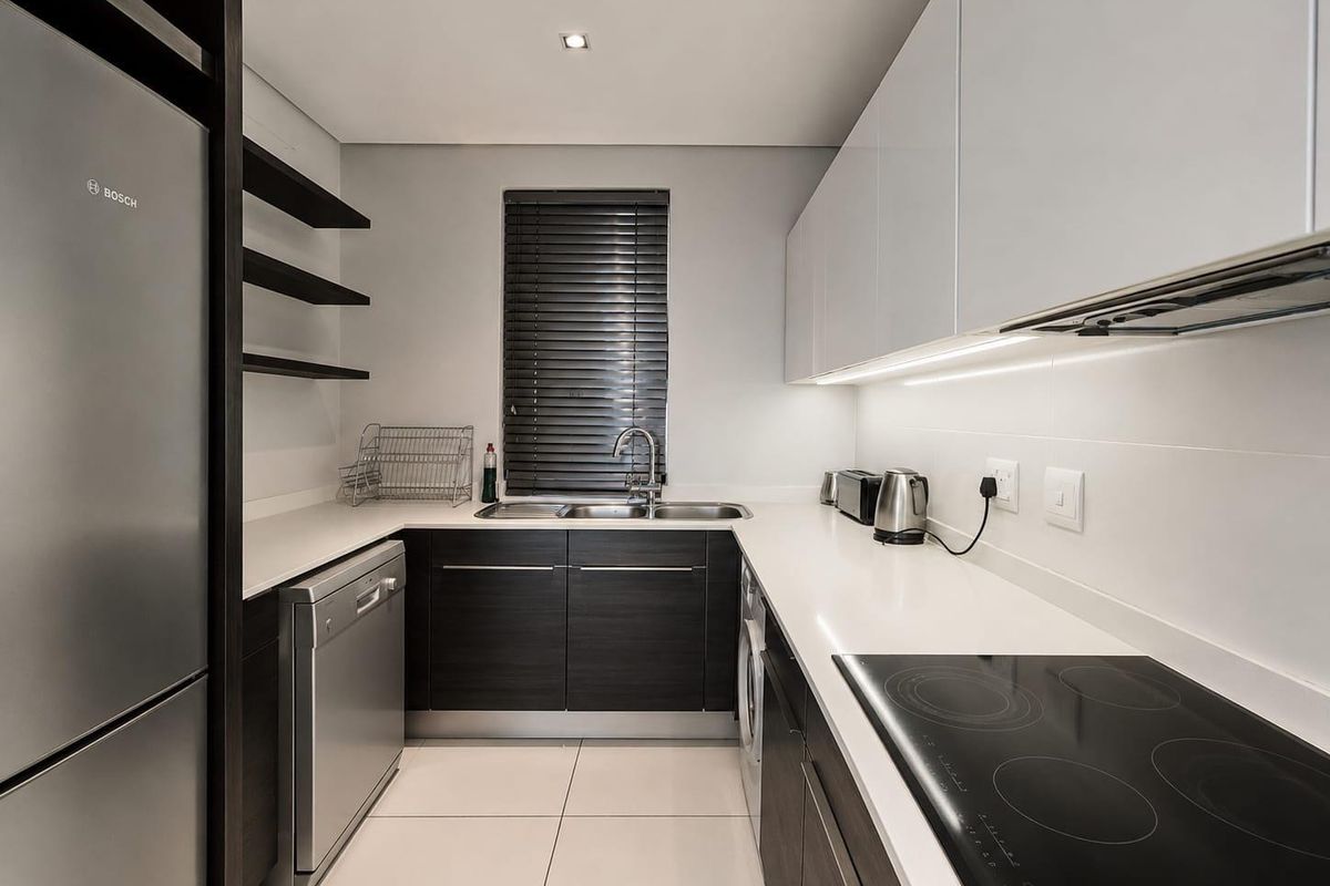 Modern kitchen featuring sleek dark cabinetry, white stone countertops, integrated appliances, and high-quality finishes with efficient under-cabinet lighting.